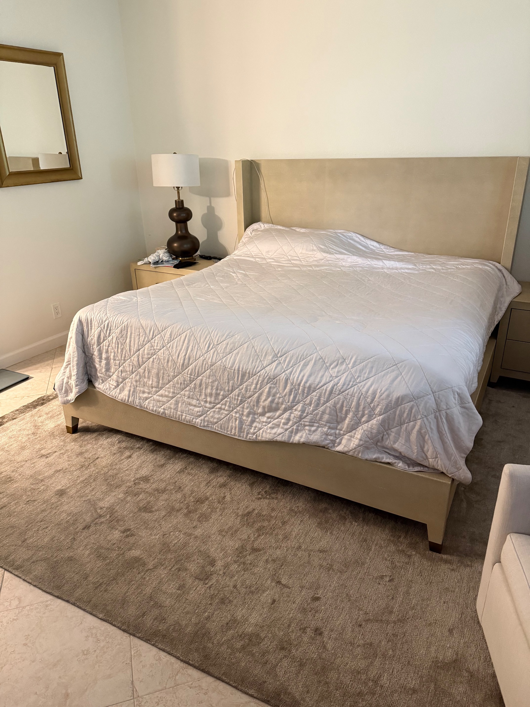 Bedroom with a large upholstered bed, white quilted comforter, bedside tables with lamp, and a wall mirror